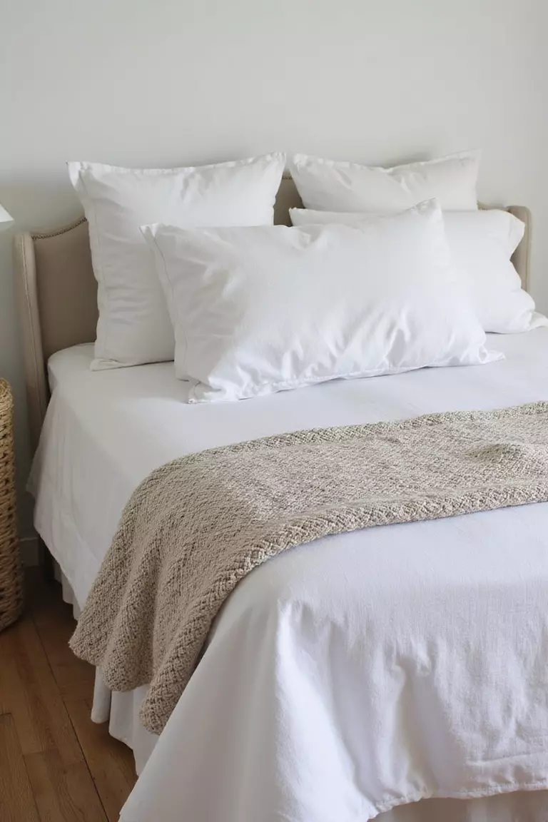 A professional photo, similar to a photo in a home design magazine, of a coastal bed dressed with layers of linen sheets, a cotton quilt, and knit throws.
