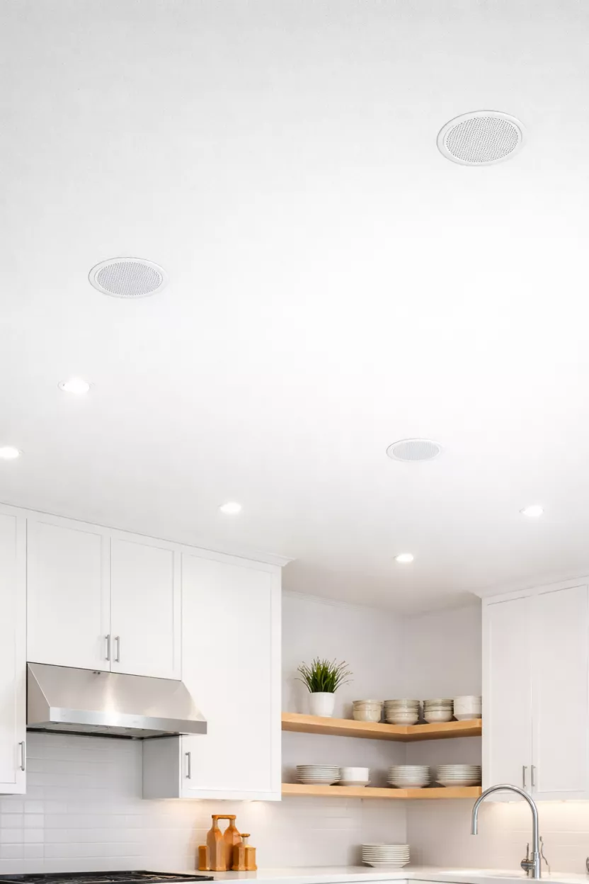 A realistic photo of a clean white kitchen ceiling with tiny flush mount speakers that blend into the surface.