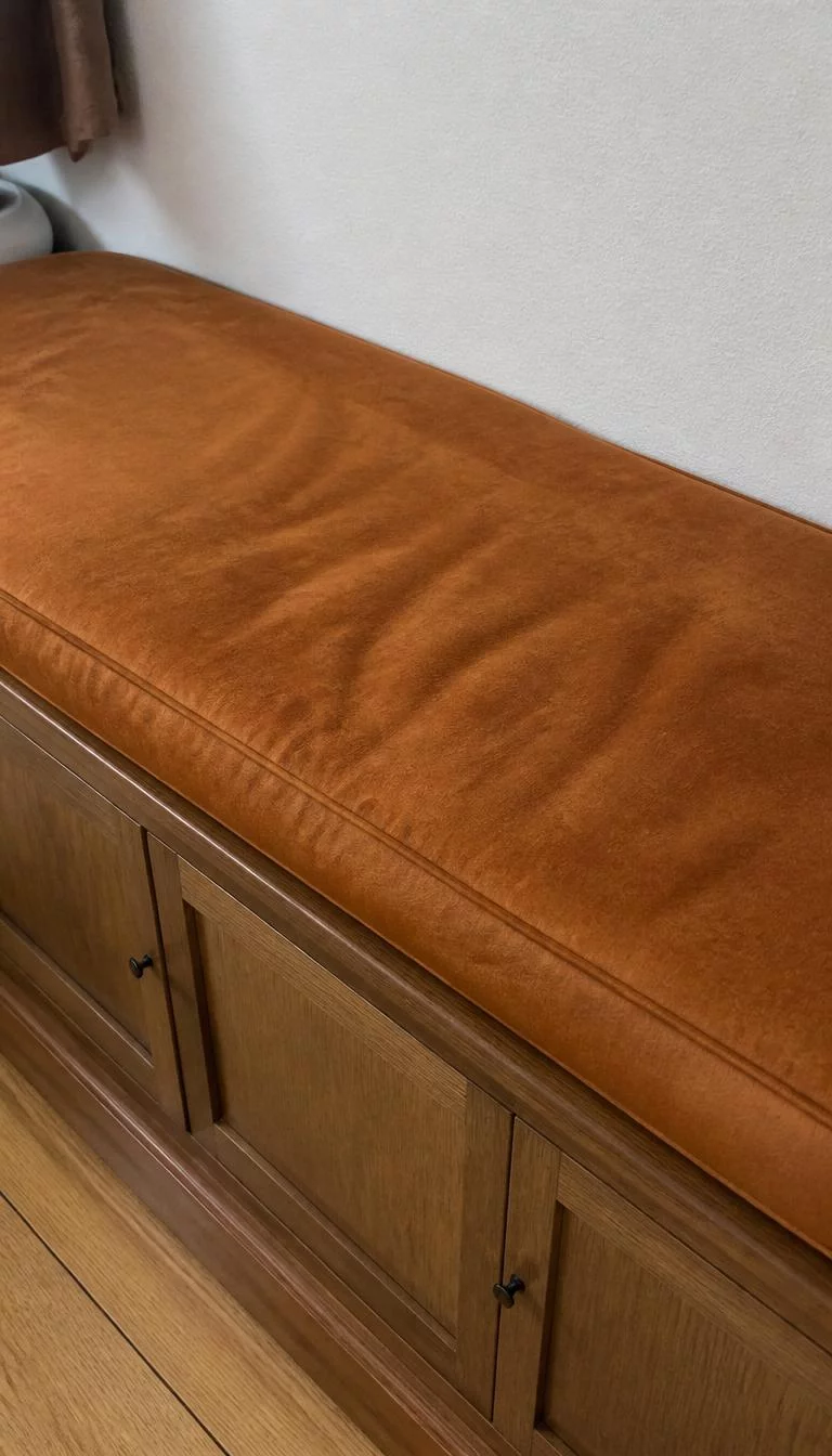 A super-realistic photo of a wooden entryway bench with a custom fitted suede cushion in a rich cognac color, showing the soft nap of the fabric and a few indentations from where someone sat, everyday social media post aesthetic, photorealistic, high-quality mobile photography, shot on an iPhone 14