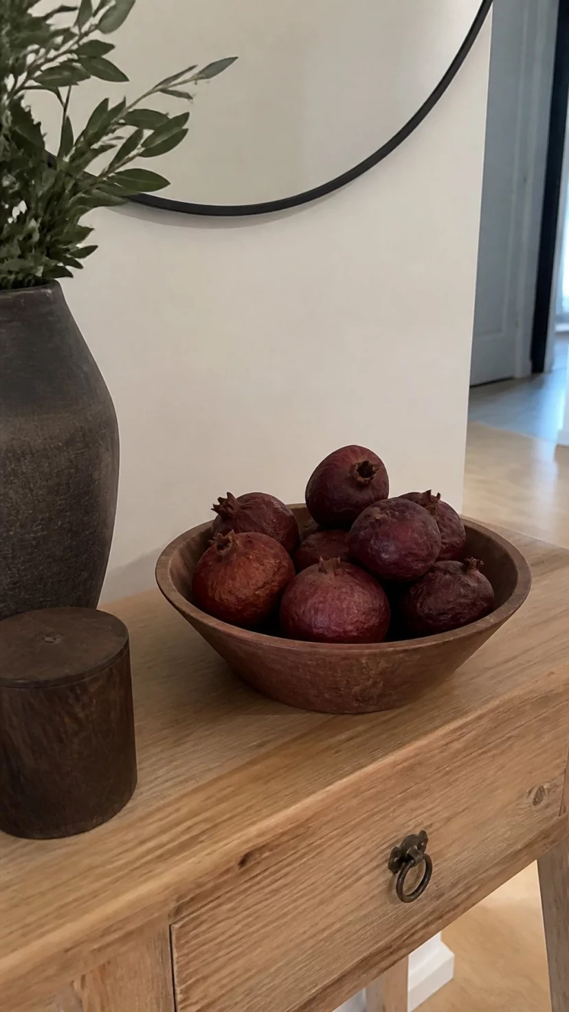 Dried Pomegranate Accents A super-realistic photo of a small entryway table with a shallow wooden bowl filled with several whole dried pomegranates in deep burgundy shades, everyday social media post aesthetic, photorealistic, high-quality mobile photography, shot on an iPhone 14
