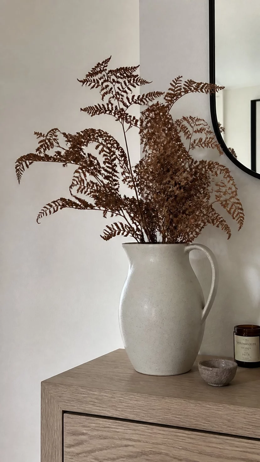 Handmade Stoneware Pitchers A super-realistic photo of a light colored entryway table with a handmade speckled stoneware pitcher used as a vase for a bunch of dried brown ferns, everyday social media post aesthetic, photorealistic, high-quality mobile photography, shot on an iPhone 14