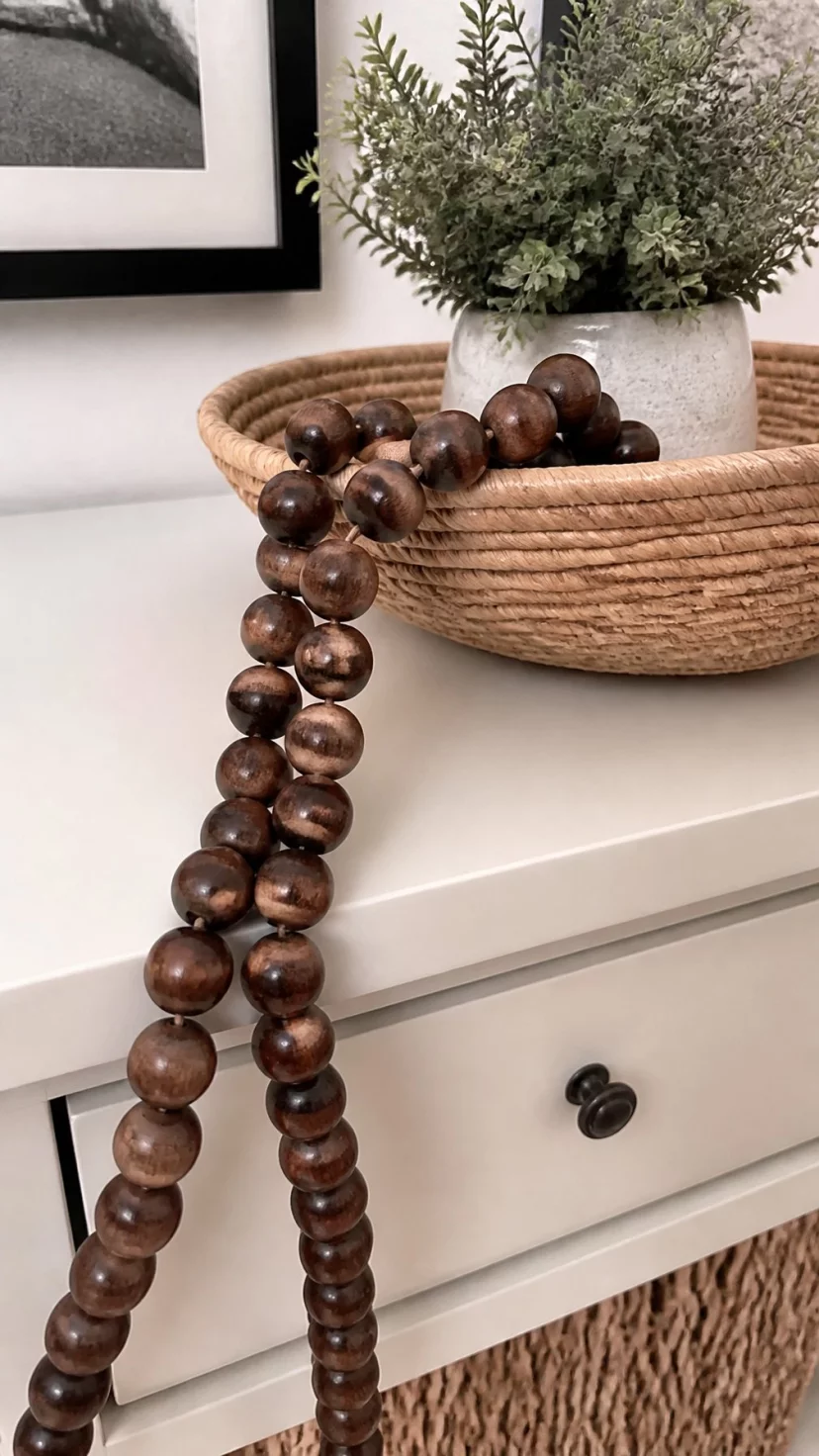 Dark Wood Beaded Garlands A super-realistic photo of a white entryway table with a long garland of chunky dark walnut wood beads draped over the corner of a large woven bowl, everyday social media post aesthetic, photorealistic, high-quality mobile photography, shot on an iPhone 14