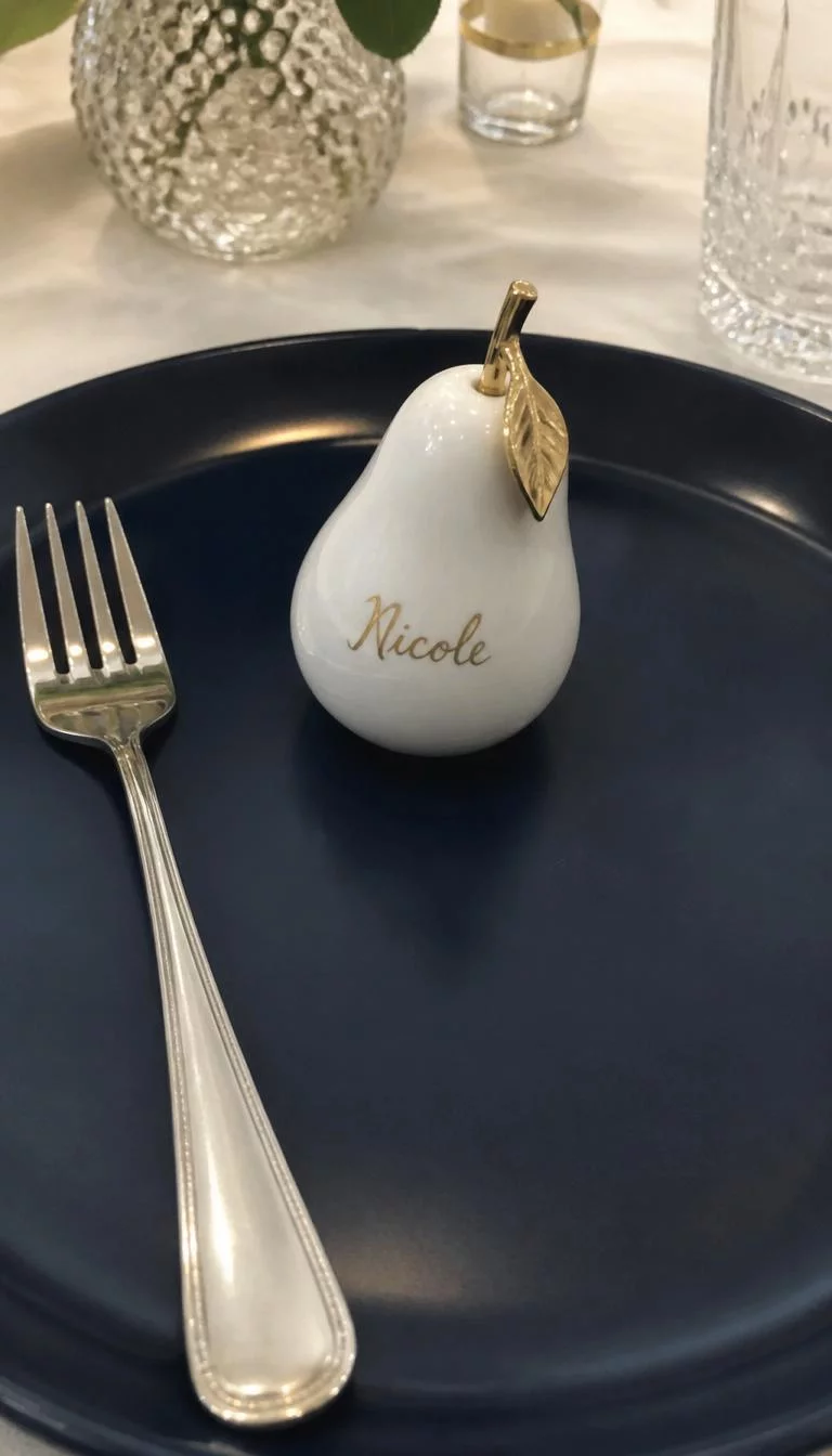 A super-realistic photo of a dining table setting where a small white ceramic pear with a guest name written in gold ink sits on a navy blue plate next to a silver fork, everyday social media post aesthetic, photorealistic, high-quality mobile photography, shot on an iPhone 14