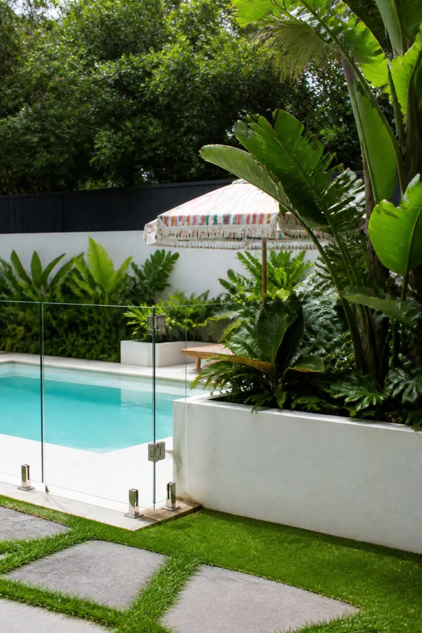 Glass Fenced Foliage Garden A realistic photo of a garden featuring a small pool enclosed by transparent glass fencing and white planters filled with dense tropical green plants and a colorful umbrella.