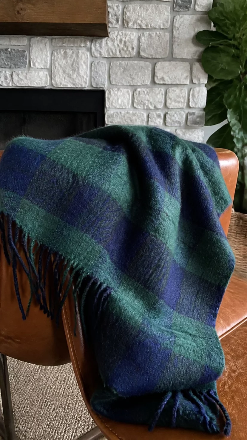 A super-realistic photo of a high-quality mohair throw blanket with a large-scale plaid pattern in navy and forest green draped over the back of a leather chair, the wool looks soft and fuzzy, everyday social media post aesthetic, photorealistic, high-quality mobile photography, shot on an iPhone 14