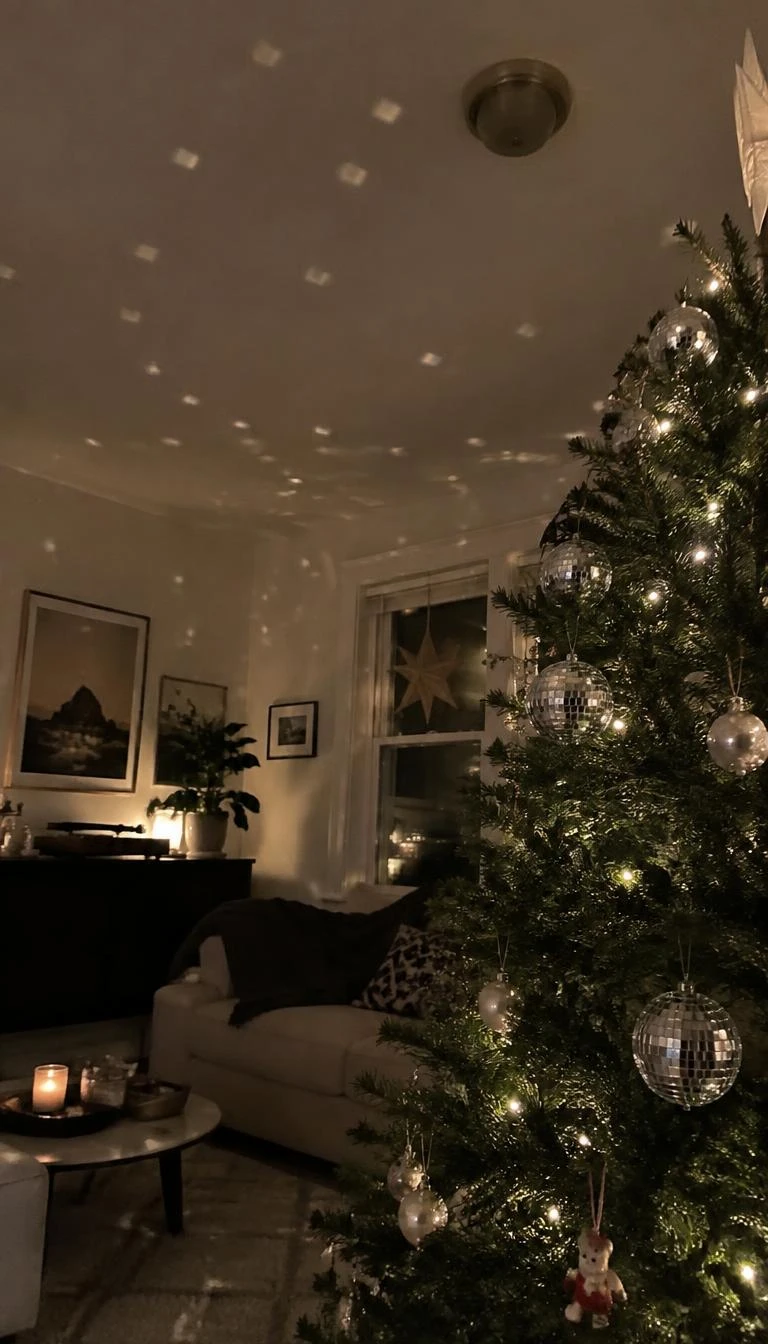 Suspend Mirrored Disco Balls for Light Reflection A candid, realistic iPhone photograph of a living room with a Christmas tree, miniature mirrored disco ball ornaments reflecting tiny dots of light across pine needles and ceiling, cozy nighttime interior.