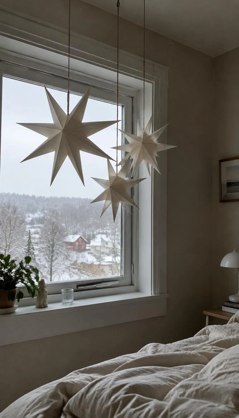 A candid, realistic iPhone photograph of a bedroom window, showing three large off-white three-dimensional paper stars hanging at varied lengths from natural twine, gentle snowy daylight outside.