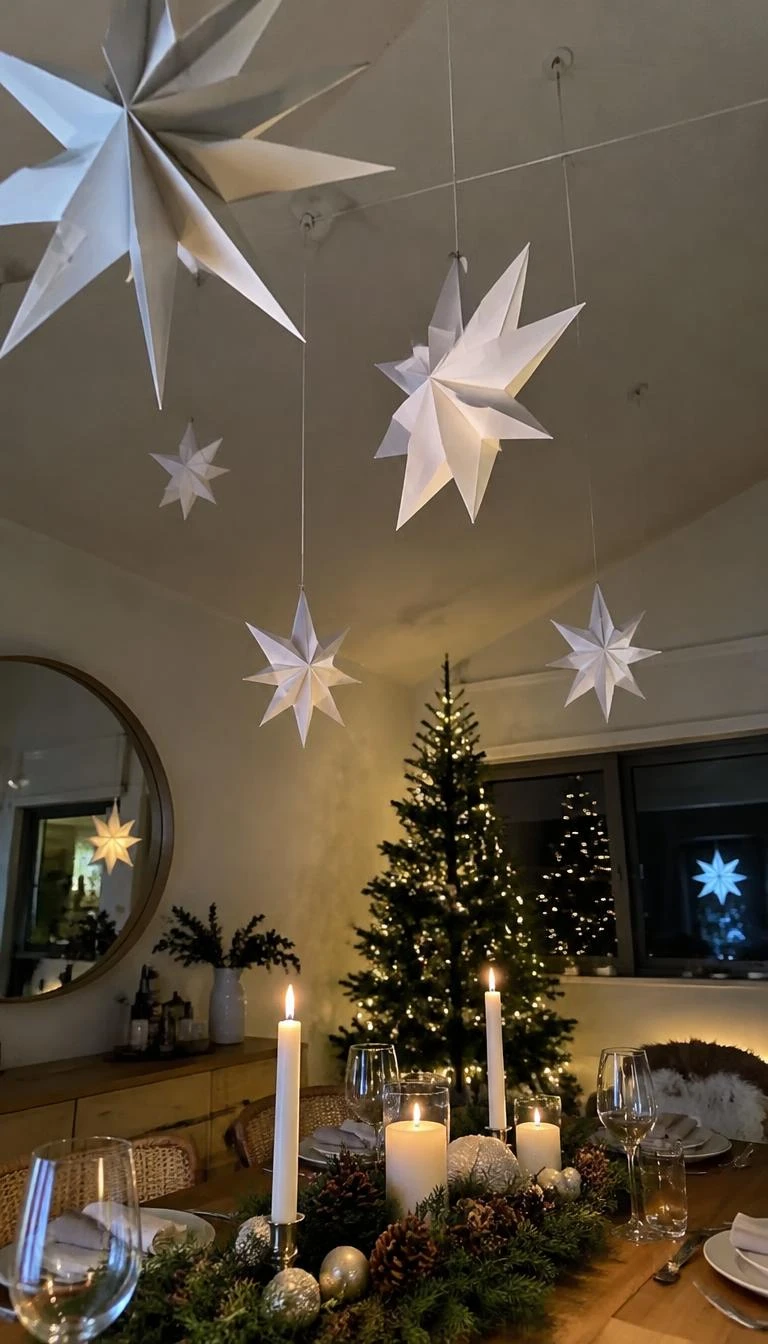 A realistic smartphone photograph of a Christmas table looking upward, showing folded white three dimensional paper stars suspended on thin cotton thread at varied heights above an arranged wooden holiday table.