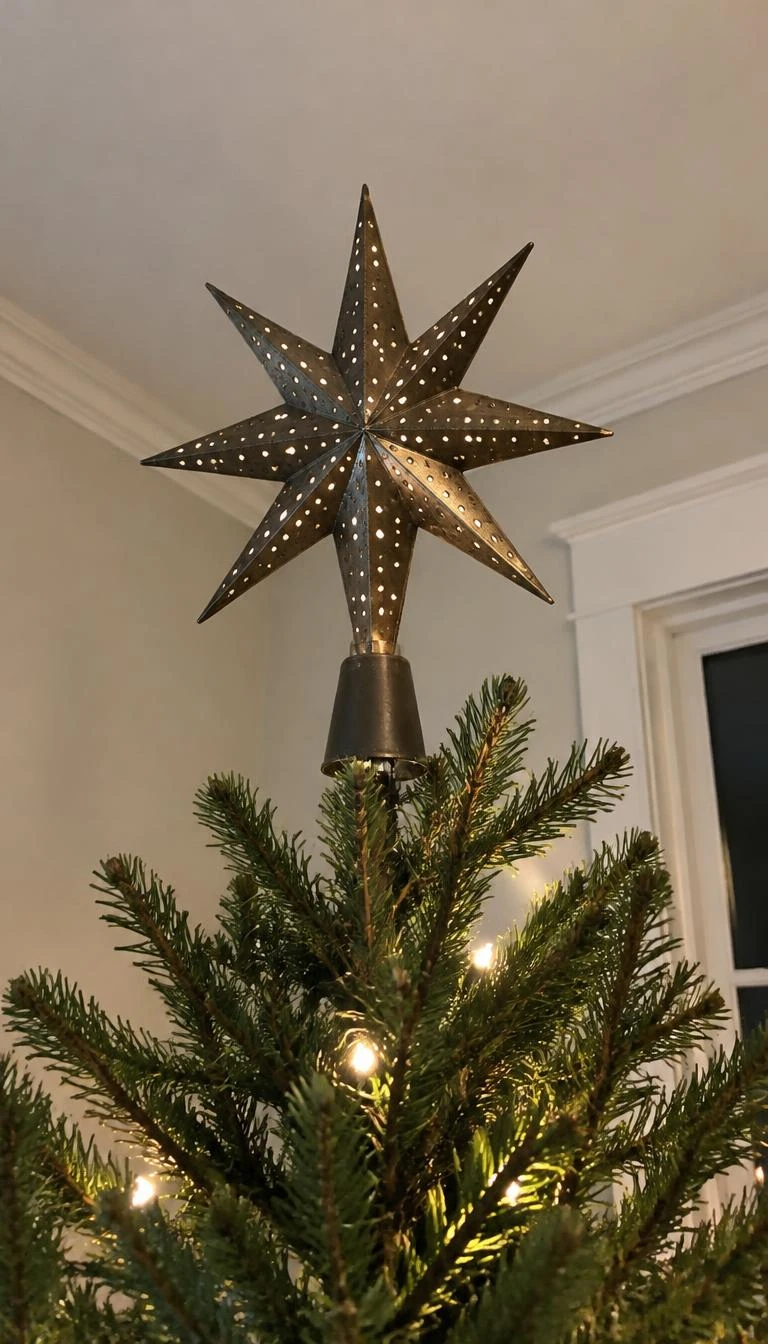 Top The Tree With An Eight Point Punched Tin Star A candid, realistic iPhone photograph of the top of a green Christmas tree, featuring an eight point punched tin star ornament, subtle metallic glint from tree lights below, natural pine needles surrounding the finial.